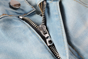 Macro shot of silver metal zipper and yellow stitching on light blue denim jeans