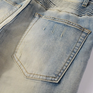 Detailed view of biker pleats and vintage distressed finish on light blue denim jeans
