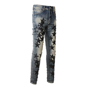 Detail of slim-fit blue jeans with black leather star patches and distressed knee rips
