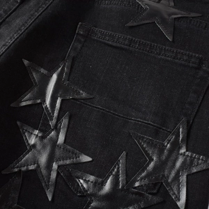 Detailed macro view of black denim jeans with stitched faux-leather star patches