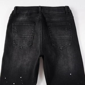 Macro detail of charcoal black distressed denim pockets with white paint splatter design