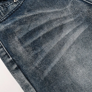 Detail shot of deep blue washed denim fabric with visible twill texture and metal rivet