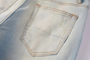 Detail of light blue vintage denim pocket with distressed texture and orange stitching