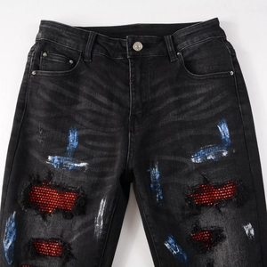 Detail view of black distressed jeans featuring red rhinestone patches and paint splatters