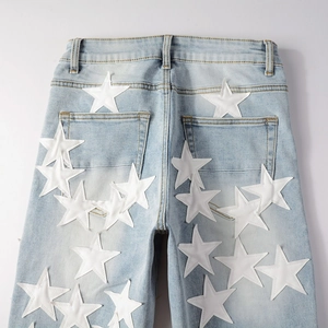Detail of light blue washed denim jeans featuring white PU star patchwork on the back pocket