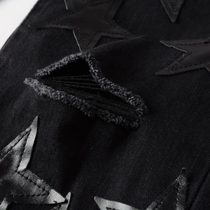 Detail of black denim jeans featuring stitched star patches and distressed ripped texture