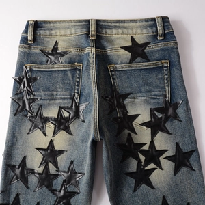 Detailed view of black leather star patches on slim-fit distressed men's denim jeans