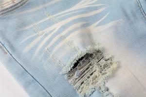 Close-up of light blue distressed denim with tiger wash and ripped patch details