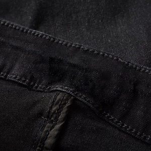 Macro view of heavy black denim fabric showing double stitching and waistband details