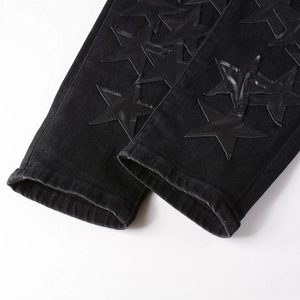 Detailed close-up of leather star patches on washed black denim jeans hemline