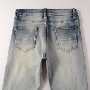 Detail of light blue washed denim jeans featuring back pockets and vintage distressed texture