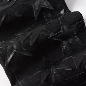 Detailed close-up of black leather star patches sewn on dark denim jeans fabric