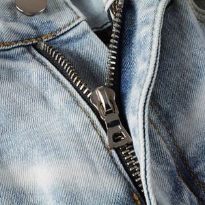 Detail of metal zipper closure and gold stitching on light blue washed denim jeans