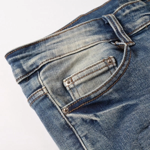 Detail of waist and coin pocket on slim fit blue jeans with faded wash and rivets