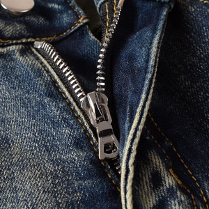 Detail of blue denim jeans showing silver metal zipper and yellow stitching craft