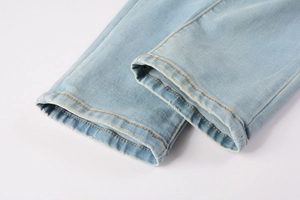 Detail shot of light blue denim jeans cuff showing orange stitching and distressed edges