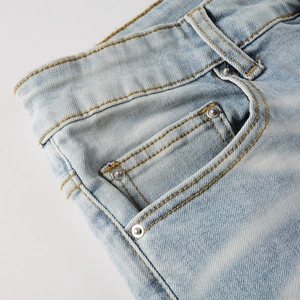 Detail of light blue denim jeans showing yellow stitching and metal rivets on the pocket
