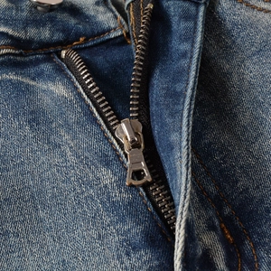 Macro detail of high-quality silver metal zipper and button on washed blue denim jeans
