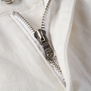 Close-up of a silver metal zipper and stitched white denim fabric on men's slim fit jeans