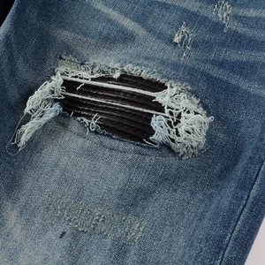 Détail d'un jean bleu délavé avec déchirures usées et empiècements en cuir noir pour homme