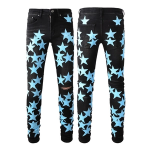 Dettaglio dei jeans slim da uomo neri con toppe a stella azzurre e strappi sulle ginocchia