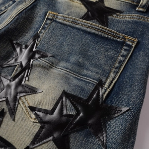 Detailed close-up of dark blue washed denim fabric with black leather star patches