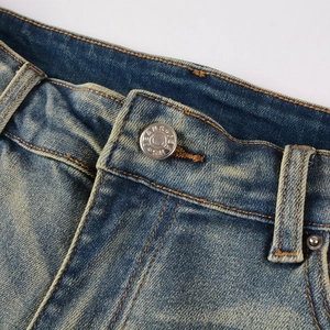 Close-up of men's blue distressed jeans waist featuring silver metal button and brown stitching