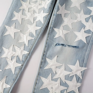 Detail of light blue denim with white star patches and distressed ripped knee effects