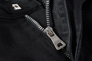 Detailed macro view of silver metal zipper and button closure on black denim jeans