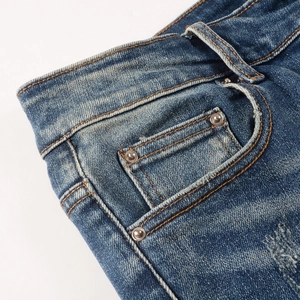 Détail d'un jean bleu délavé avec effets de moustaches et rivets métalliques