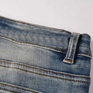 Detail of blue denim jeans waist with orange contrast stitching and blank leather patch