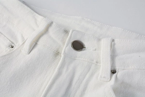 Close-up of white slim fit jeans featuring silver button and detailed topstitching textures