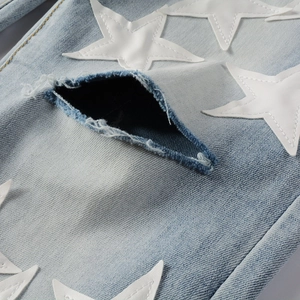Detailed close-up of light blue jeans featuring white star patches and distressed diamond rip