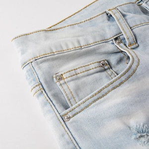 Détail du denim délavé bleu clair avec coutures jaunes, rivets en métal et bords effilochés