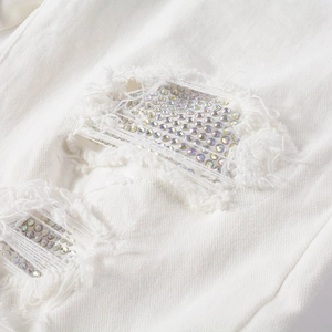 Macro view of distressed white denim with sparkling rhinestone patches and ripped texture