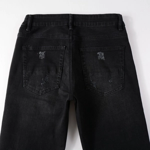 Detail of black streetwear jeans featuring distressed back pockets and paisley patch accents