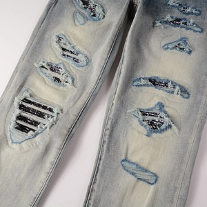 Close-up of distressed light blue jeans featuring paisley bandana patches and ripped details