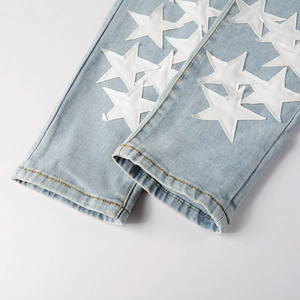 Detail view of light blue denim jeans showing white PU star patches and stitching on hem