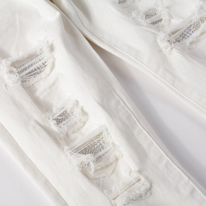 Detail of white stretch jeans with distressed ripped holes and colorful rhinestone patches