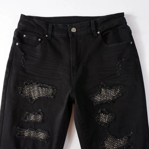 Close-up of black street style denim pants with decorative silver rhinestones and ripped details