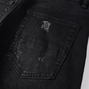 Close-up of distressed back pocket detail on black denim jeans with ripped texture