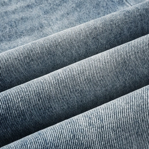 Detailed close-up of light blue stonewashed denim fabric with clear twill texture