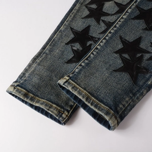 Detail of slim-fit jeans featuring vintage wash denim and black leather star patches