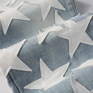 Macro detail of white star leather patches stitched on light blue washed denim fabric