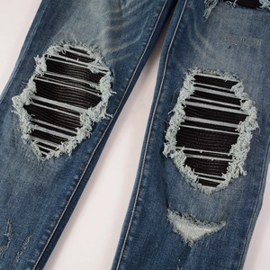 Detail of vintage washed blue jeans featuring distressed holes and striped fabric patches