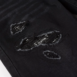 Detail shot of distressed black denim with paisley pattern patches and frayed hole design