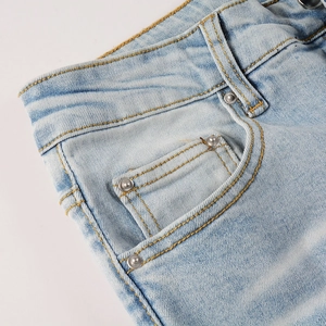Détail d'un jean bleu clair délavé avec rivets argentés et surpiqûres jaunes