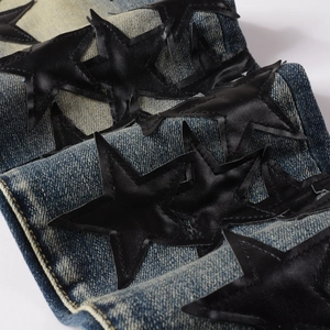 Detail of dark blue denim jeans with black leather star patches and yellow stitching