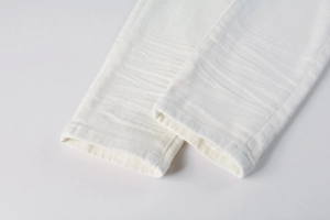Detailed close-up of white stretch denim pants leg featuring subtle whiskering effects