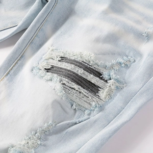 Détail d'un jean bleu clair vieilli avec écusson en rayures et bords effilochés